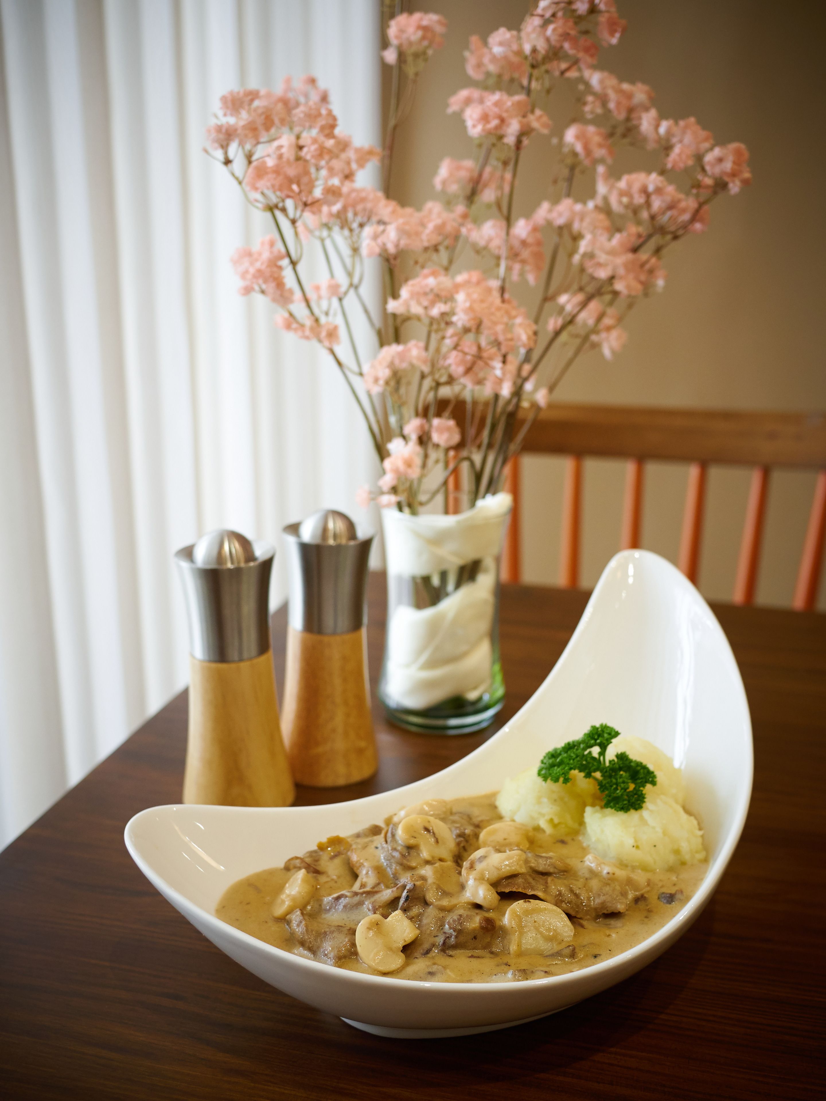 Un bol de soupe crémeuse aux champignons, accompagné d’une portion de purée de pommes de terre et d’une garniture, le tout posé sur une table en bois.