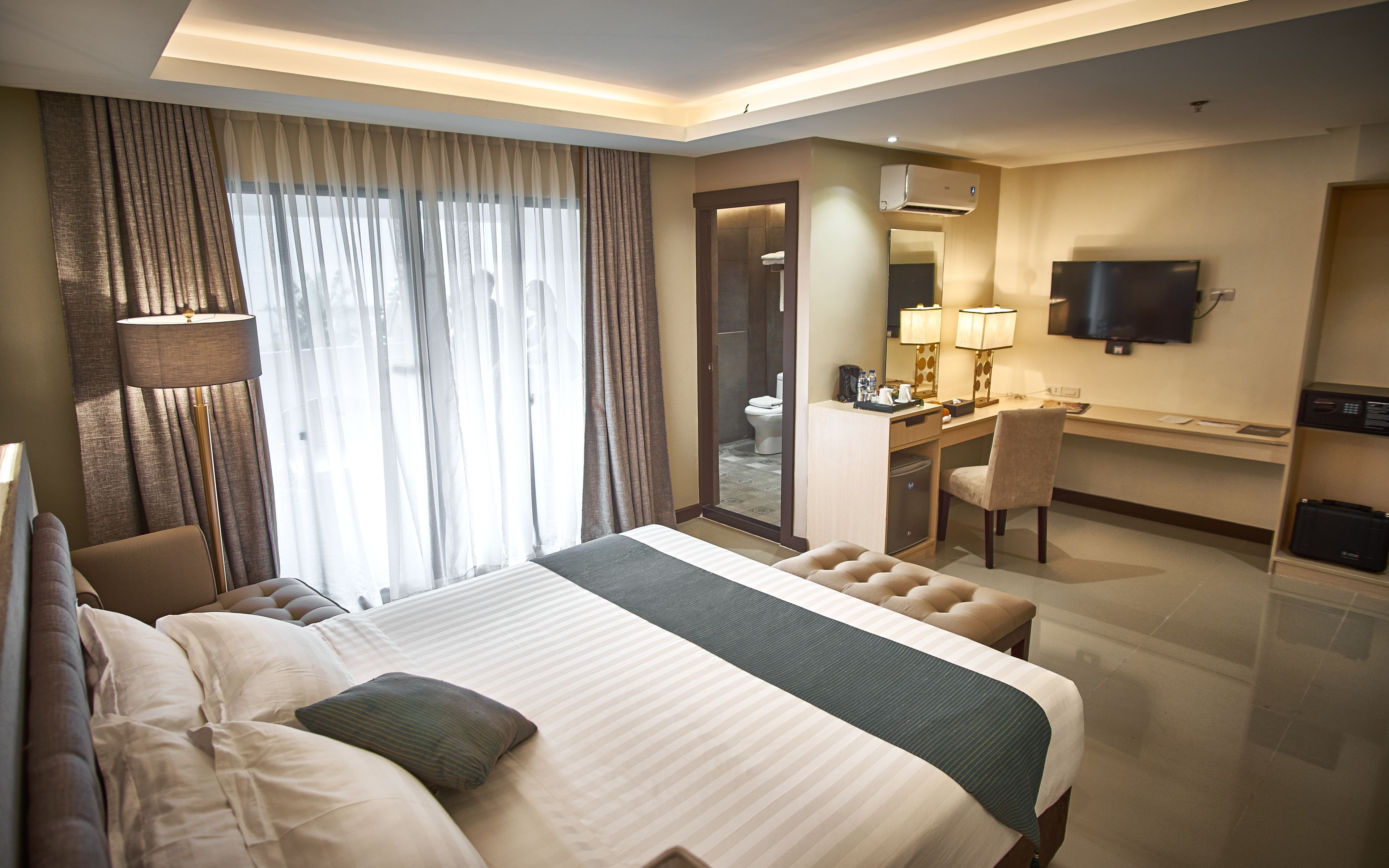 A hotel room with a large bed, a desk, a chair, a television, and a bathroom visible through an open door.