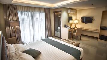A hotel room with a large bed, a desk, a chair, a television, and a bathroom visible through an open door.