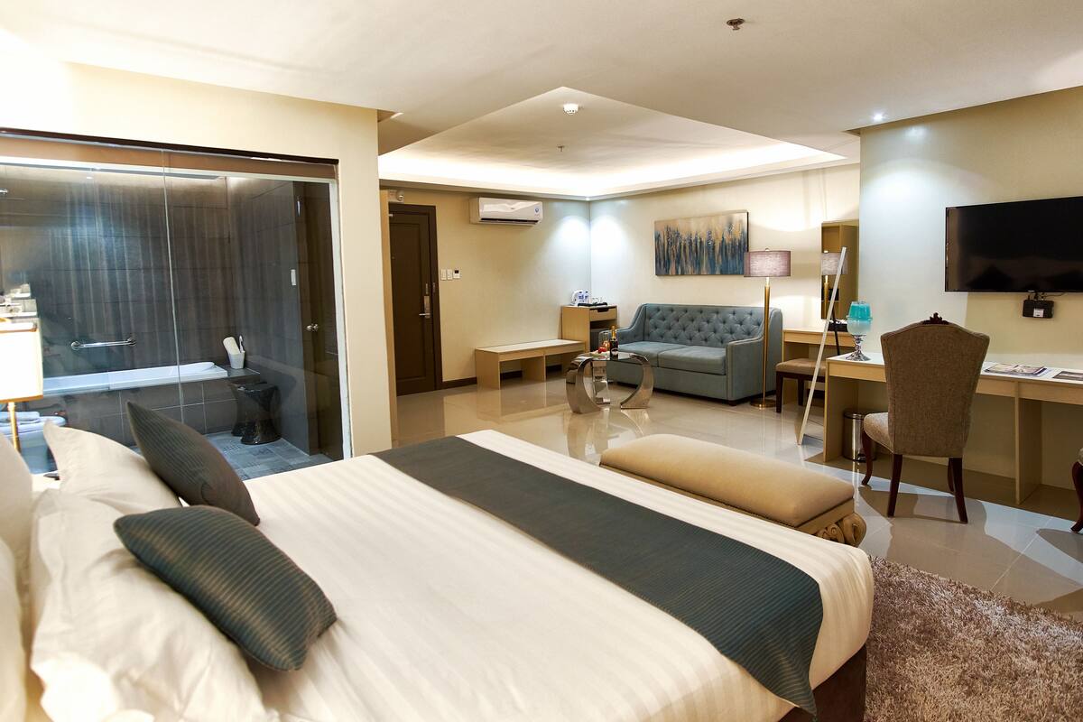 A hotel room with a large bed, a desk, a sofa, and a TV.