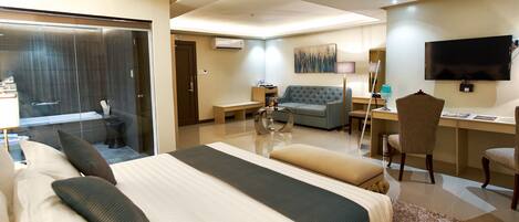 A hotel room with a large bed, a desk, a sofa, and a TV.