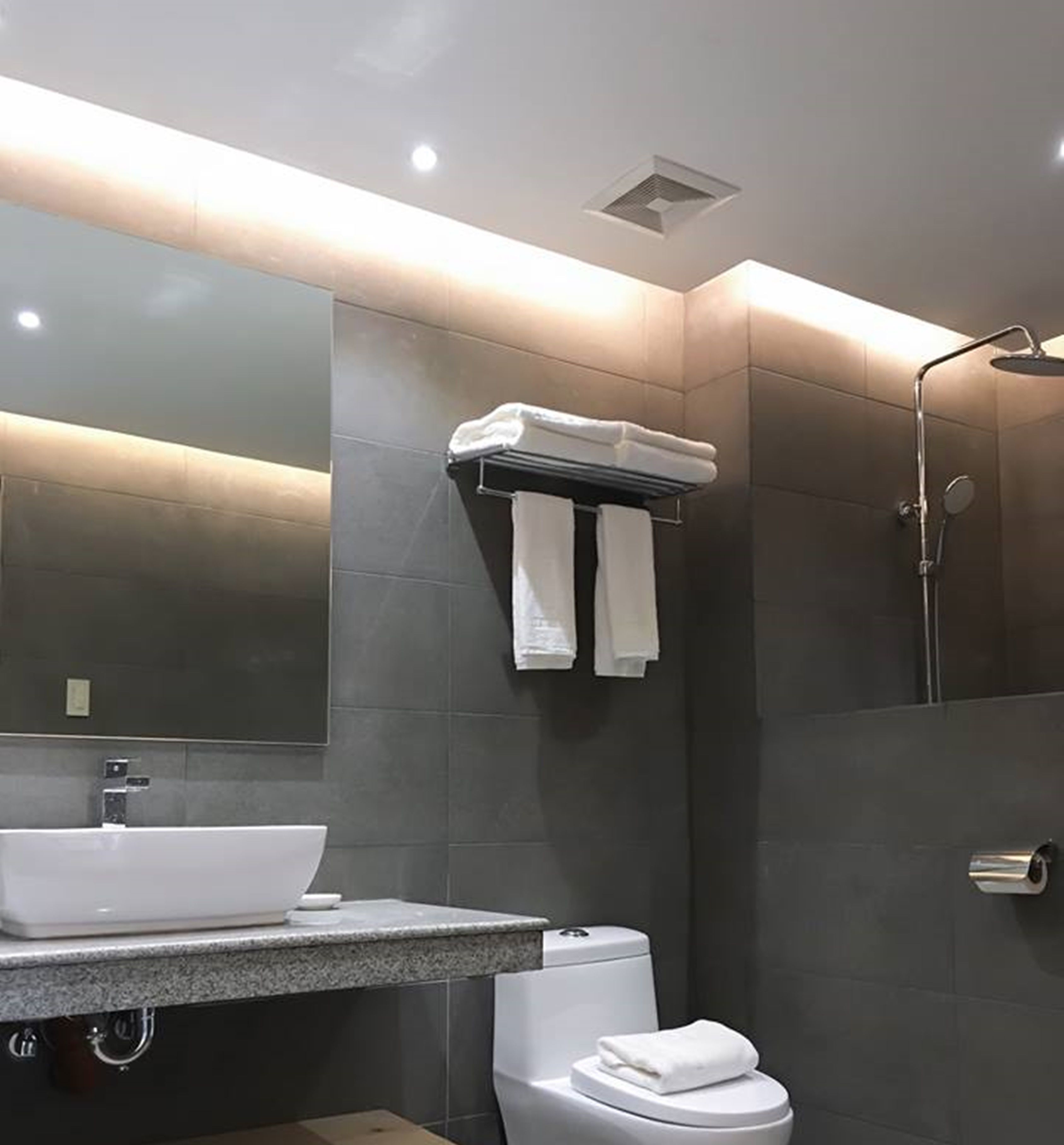 A modern bathroom with a large mirror, a sink, a toilet, and a shower.