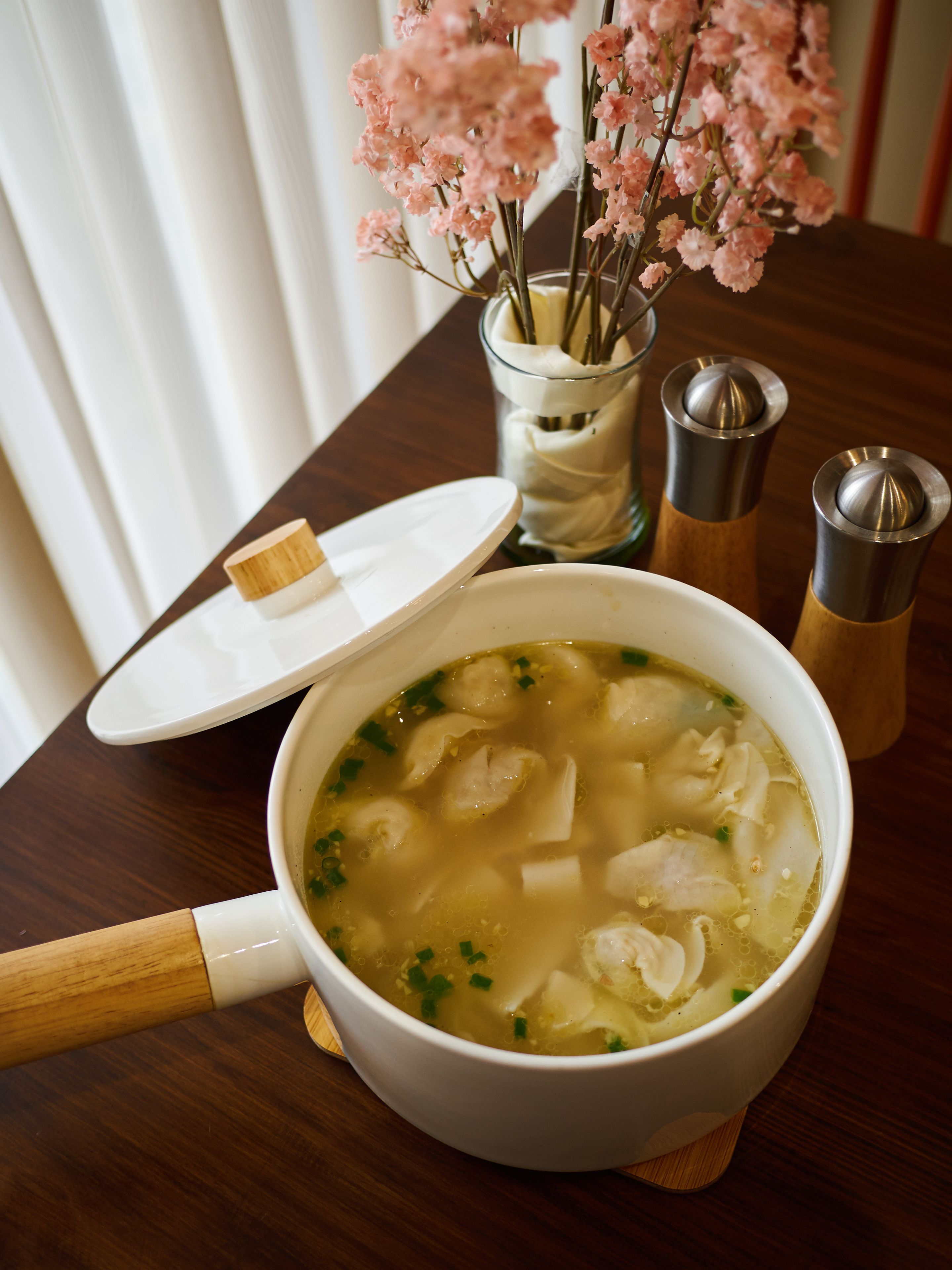 A bowl of soup with chopsticks and a spoon on a wooden table.