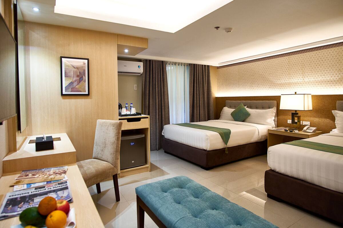 A hotel room with a bed, a desk, a chair, a small table with fruits, and a television.