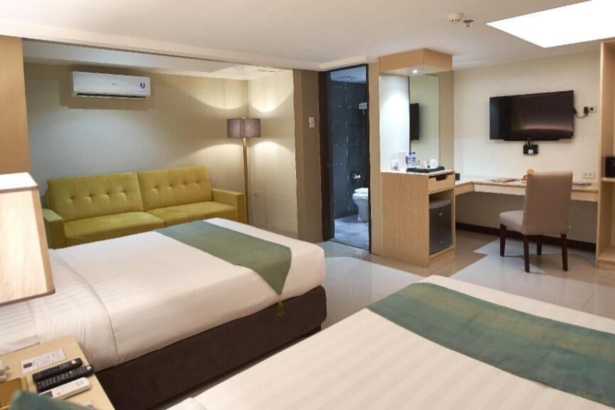 Habitación de hotel con dos camas, un sofá, un escritorio, una silla, un televisor y un equipo de aire acondicionado.