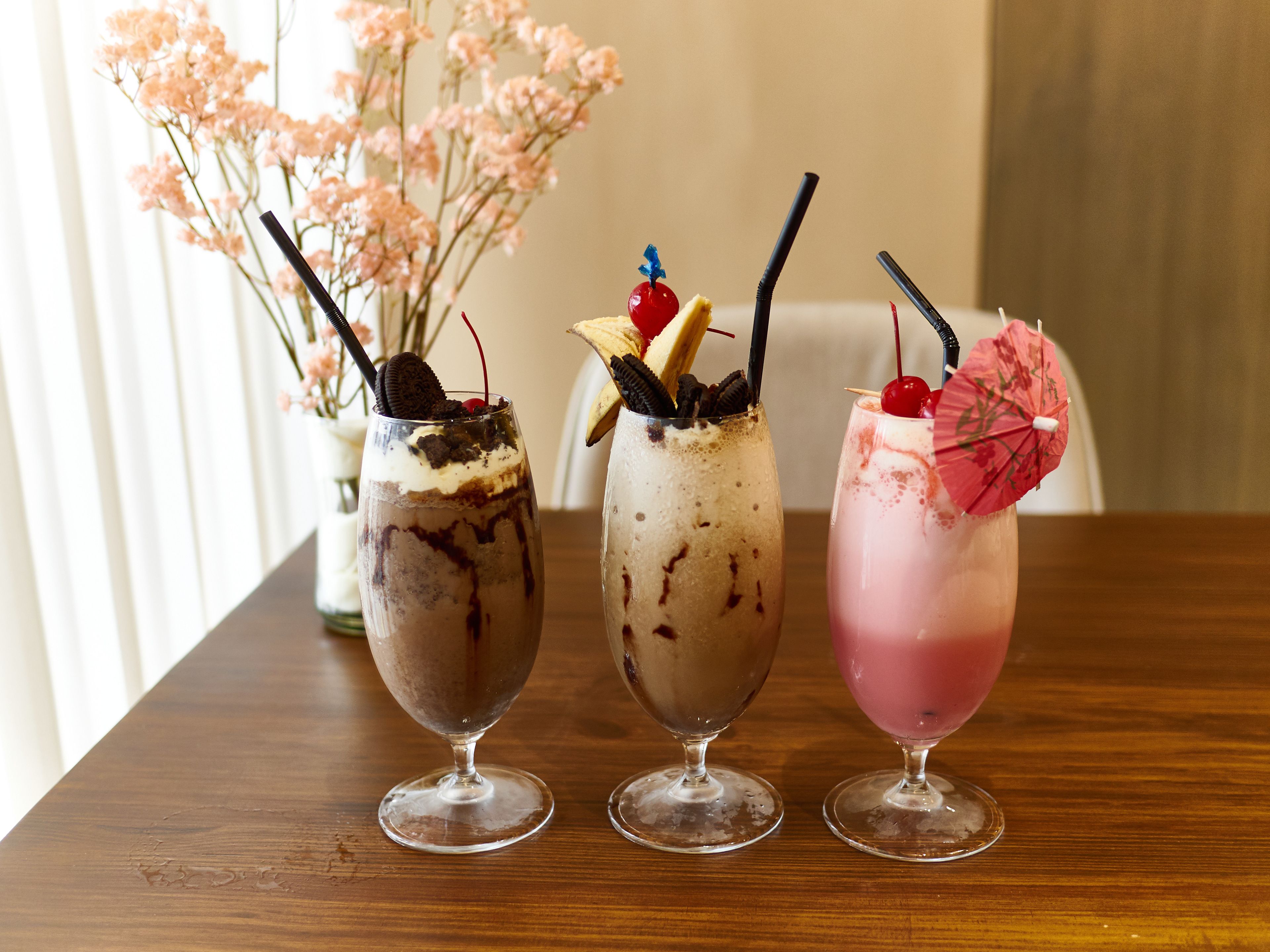 Trois verres sur une table en bois, avec un vase de fleurs en arrière-plan.