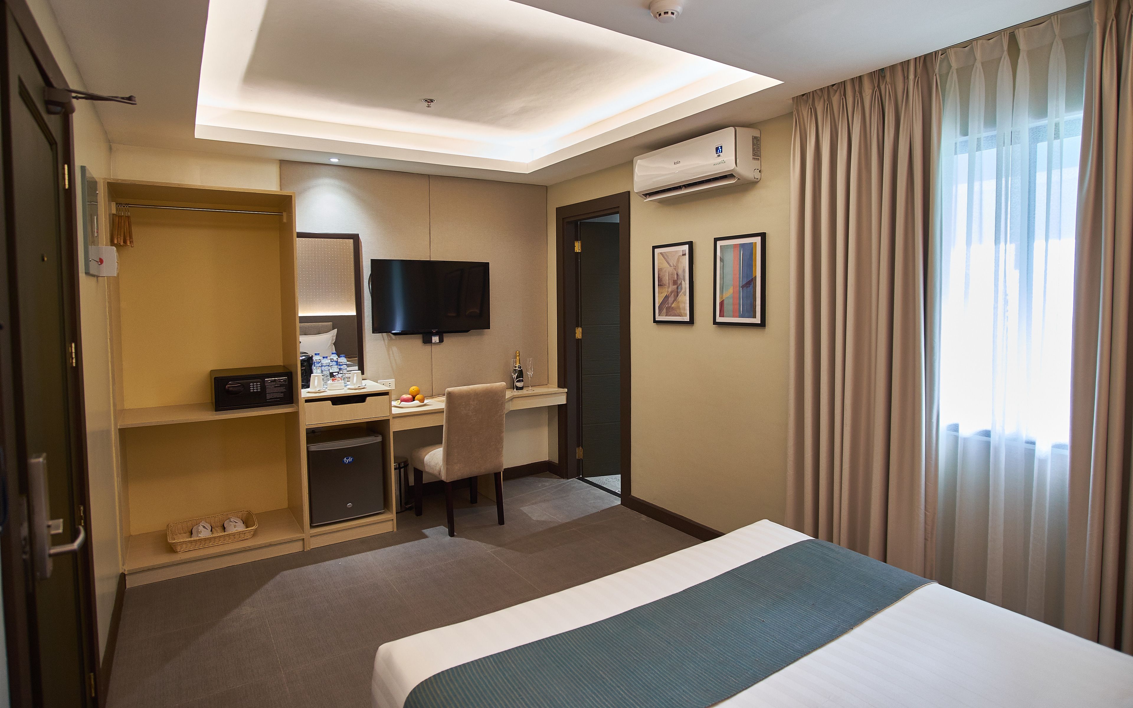 Habitación de hotel con cama, escritorio, silla, televisión, armario y aire acondicionado.