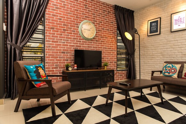 A living room with a brick wall, a television, a sofa, a coffee table, and a patterned rug.