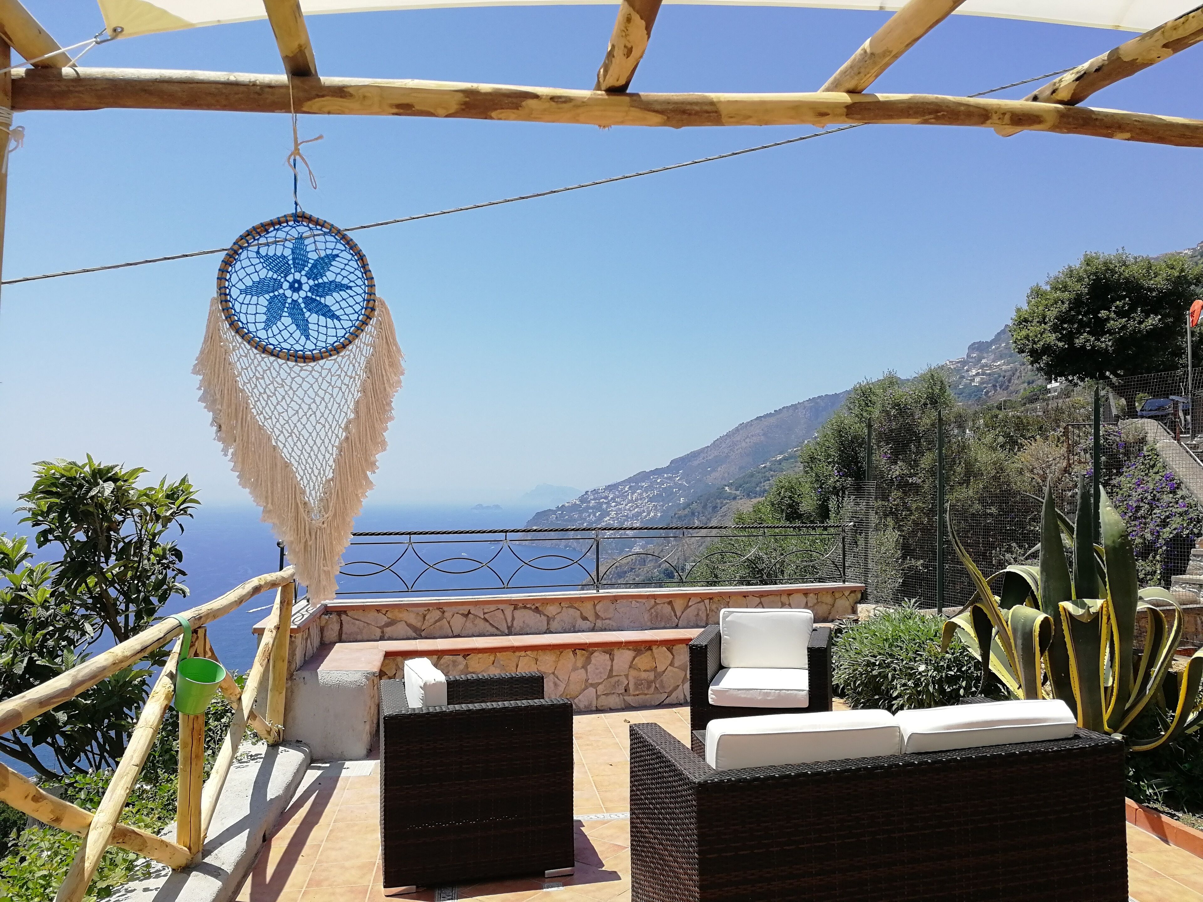 Une terrasse dotée de meubles en osier, d’un attrape-rêves et offrant une vue sur la mer et les montagnes.