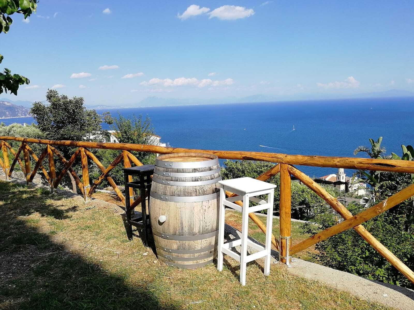 Un espace extérieur rustique aménagé avec un tonneau en bois et un tabouret blanc, offrant une vue sur la côte.