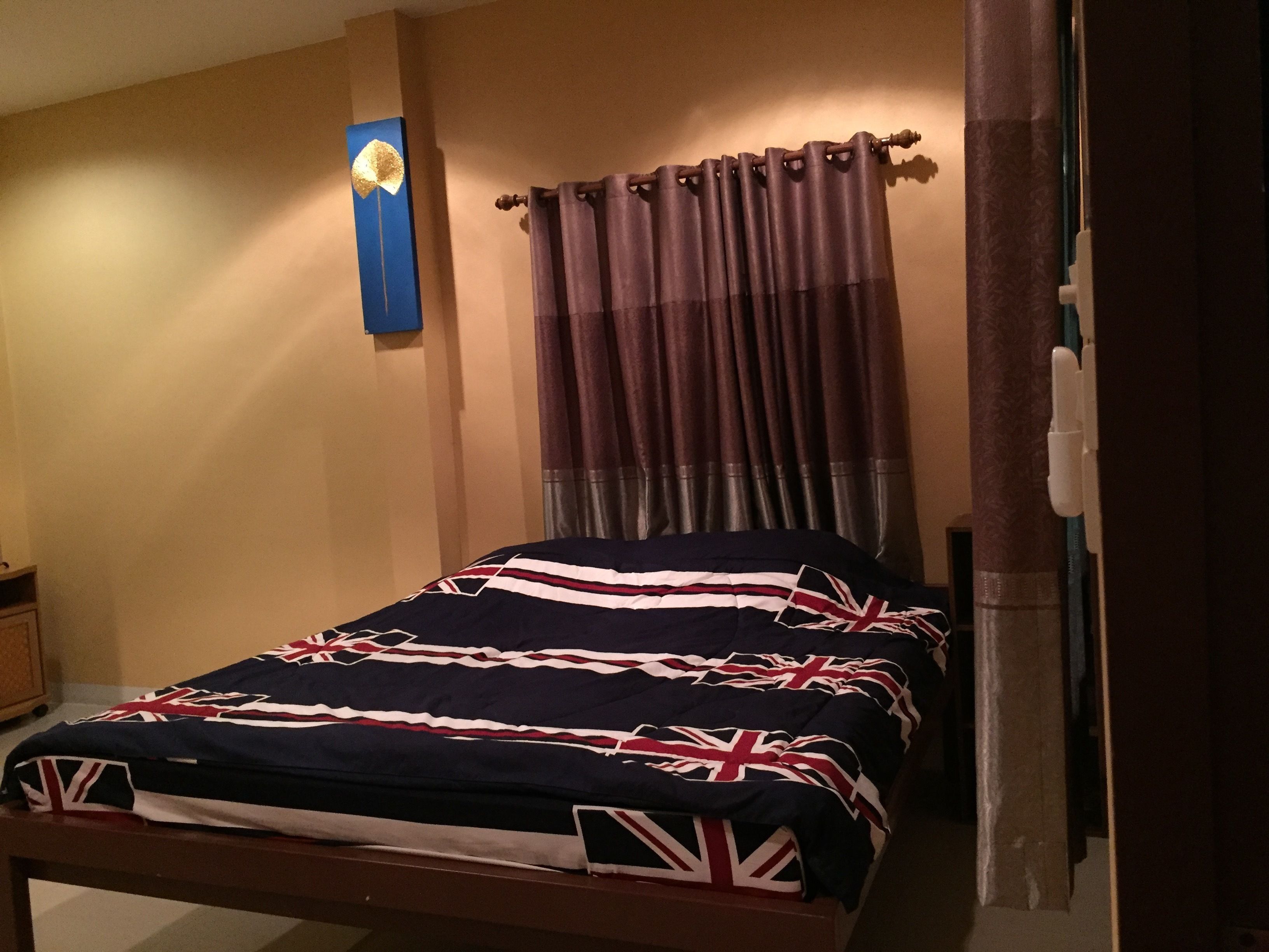 A bedroom with a bed featuring a British flag design, a curtain, and a wall-mounted light fixture.