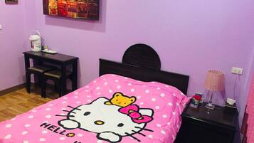 Une chambre avec une couette Hello Kitty rose, un bureau avec une lampe et une table de chevet avec une lampe.
