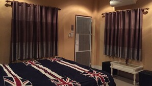 Habitación de hotel con cama, cortinas, unidad de aire acondicionado, una mesita y un espejo.
