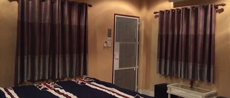 A hotel room with a bed, curtains, an air conditioning unit, a small table, and a mirror.