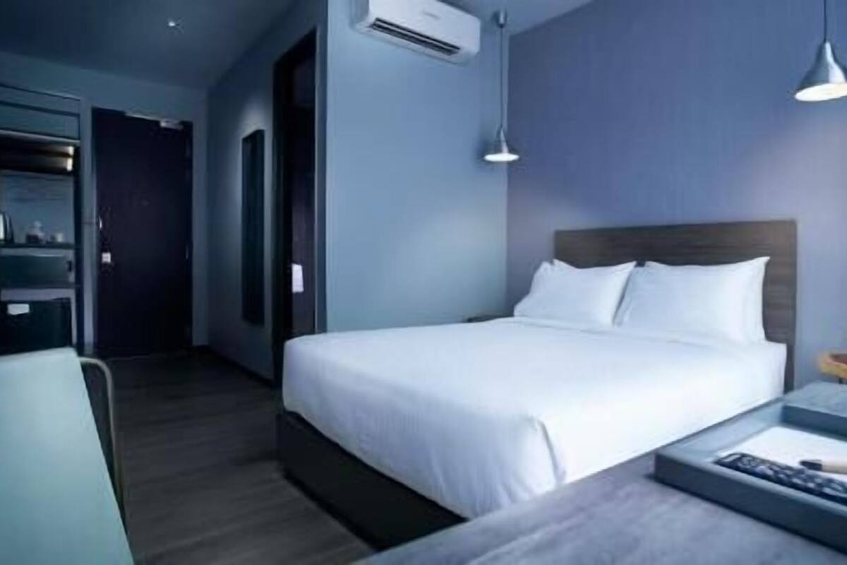 A hotel room with a bed, bedside table, lamp, and a view of the hallway.