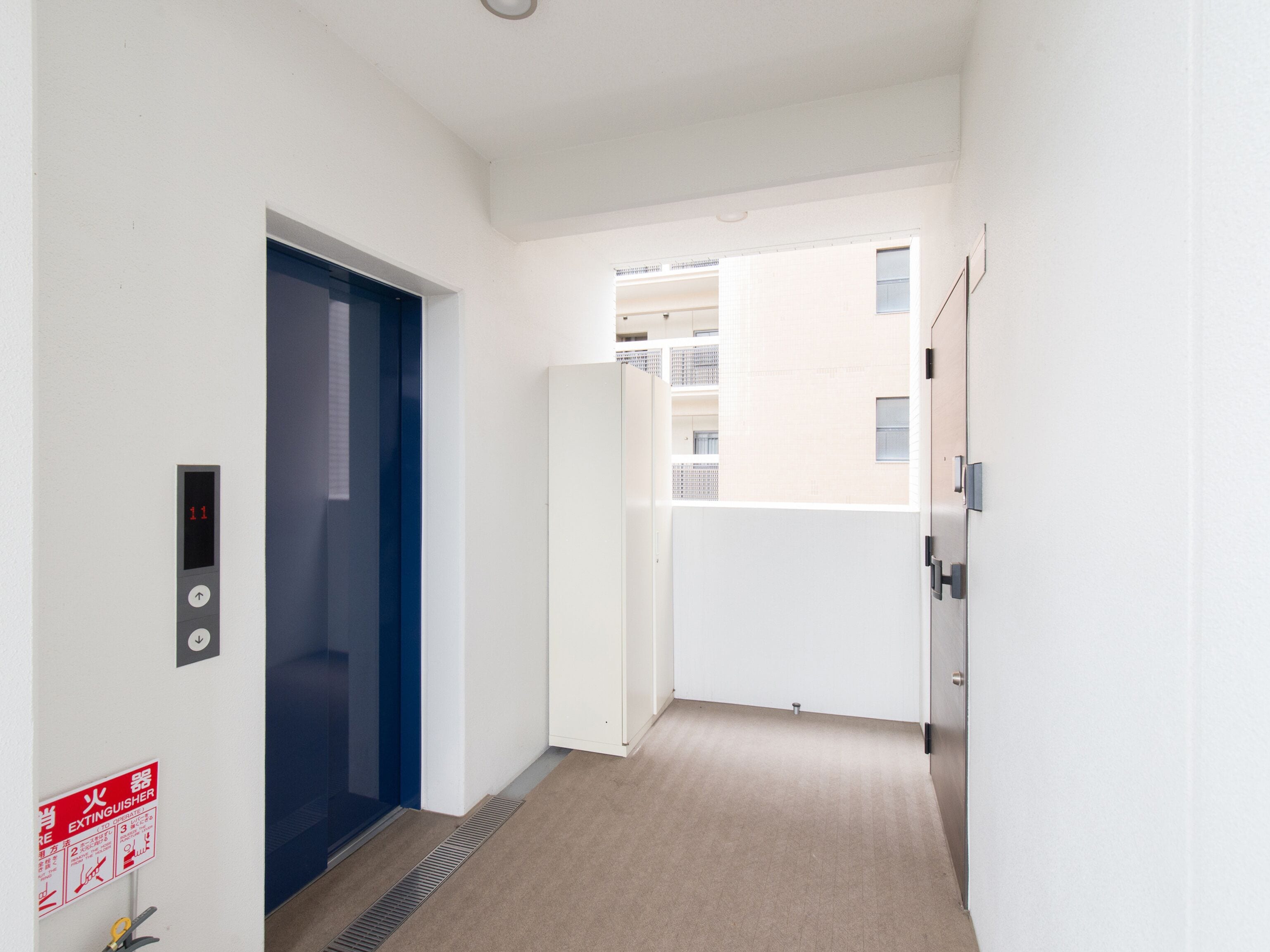 A hallway with a blue door, a fire extinguisher sign, and a vent on the floor.