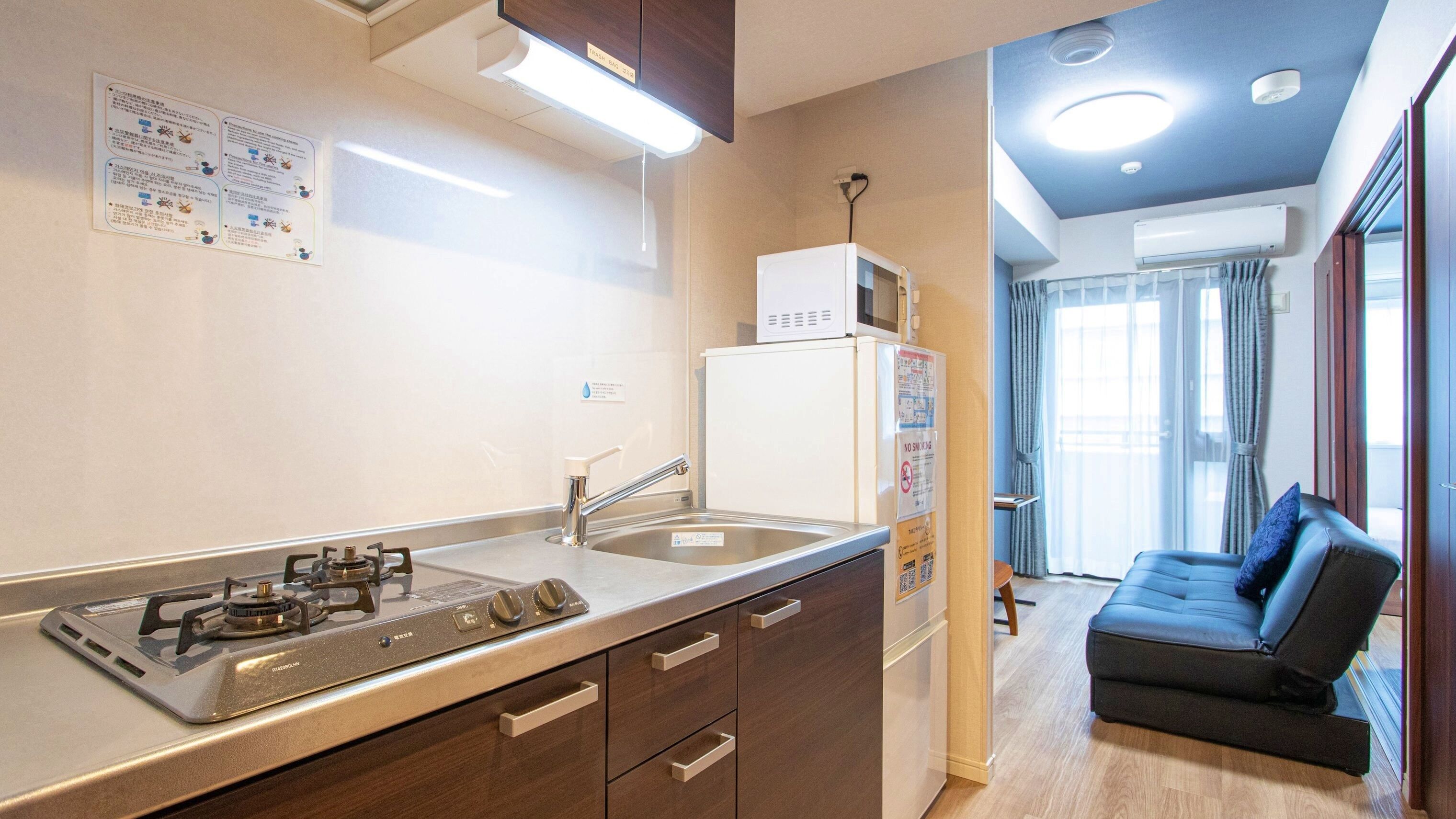 A compact kitchen with a gas stove, sink, and a refrigerator. There is a small dining area with a sofa and a window.