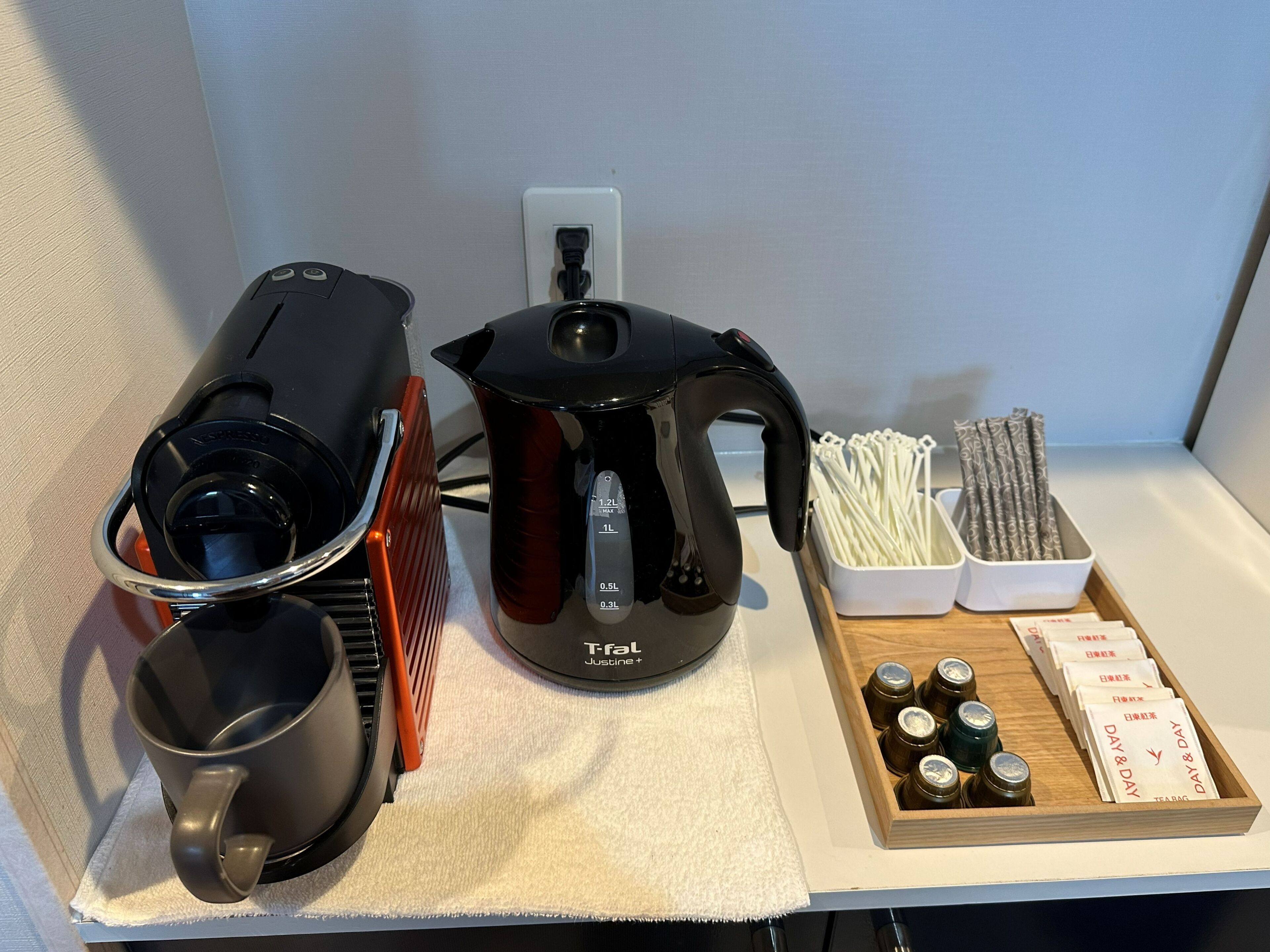 A kitchen area with a coffee maker, a kettle, a tray with tea bags, and a container of chopsticks.