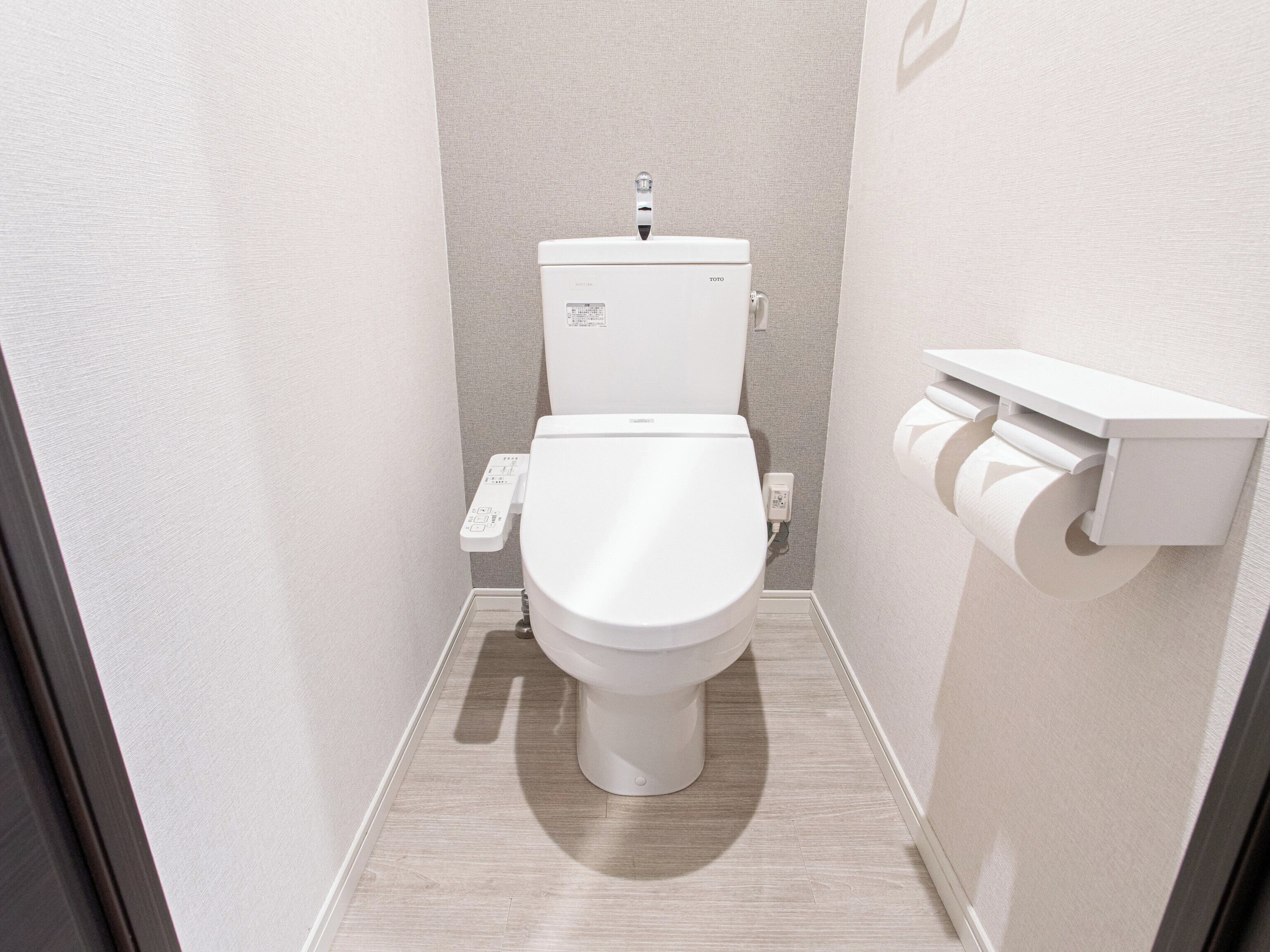 Een moderne badkamer met een wit toilet, een toiletrolhouder aan de muur en een bedieningspaneel aan de linkerkant.