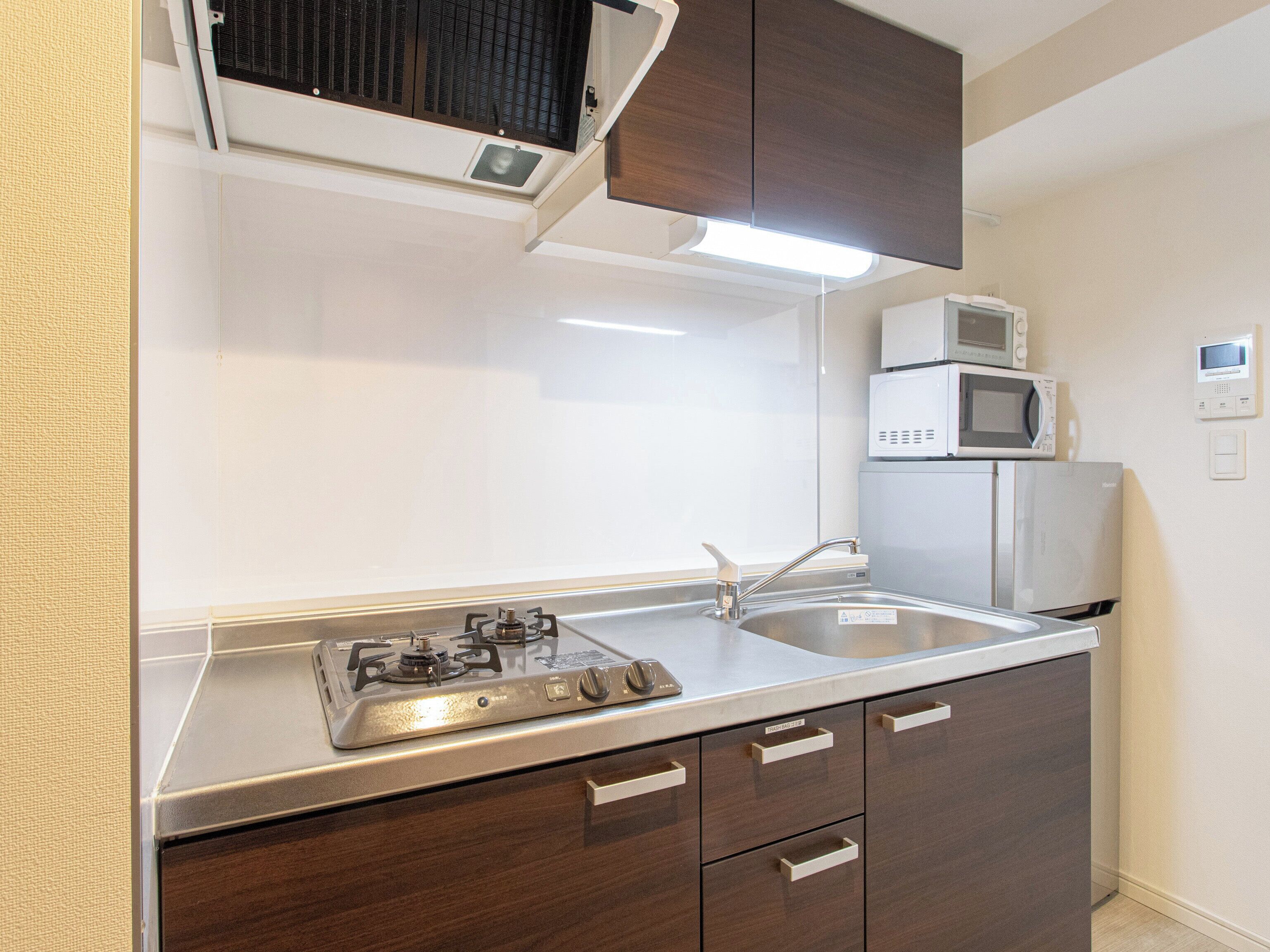 Cocina compacta con estufa a gas, pileta de acero inoxidable y dos microondas empotrados.