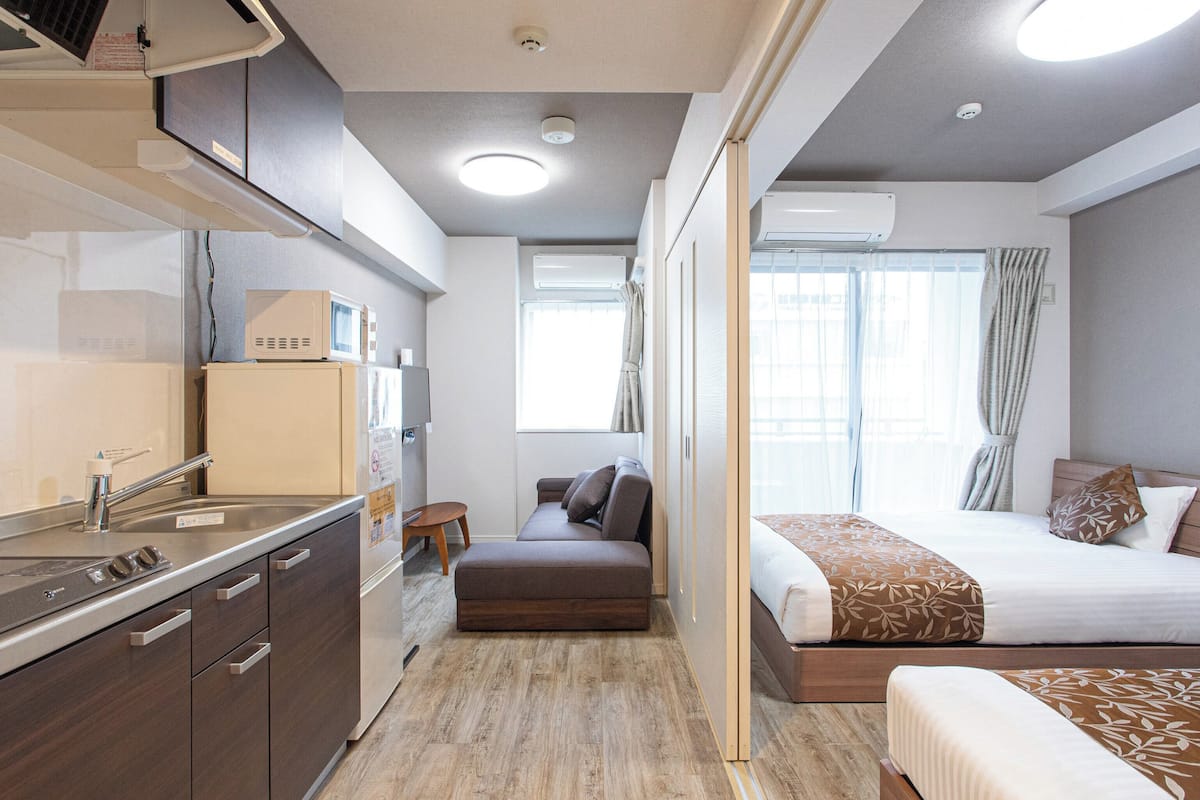Een compacte kamer met kitchenette, een bed, een klein zithoekje en een raam met gordijnen.