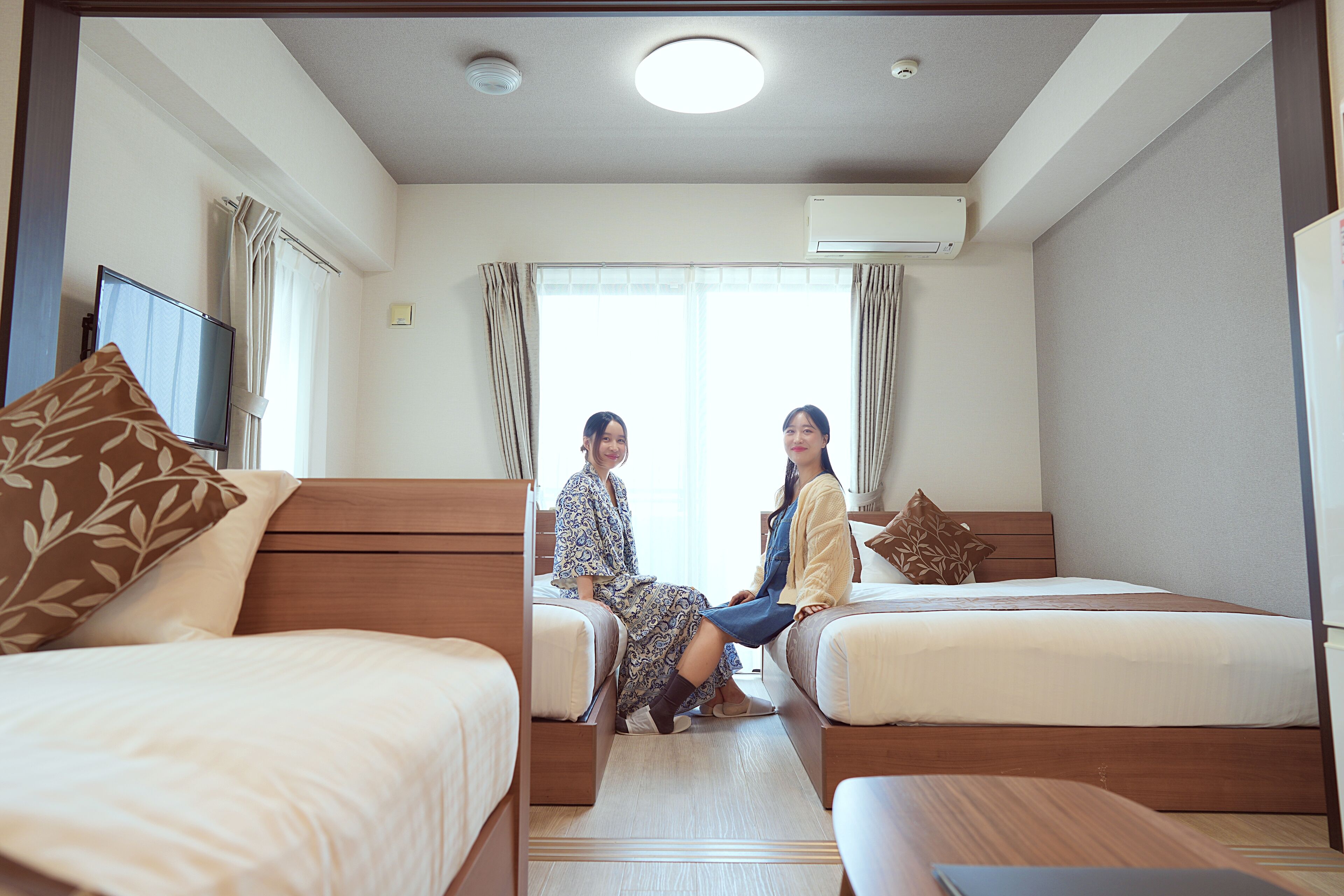 Quarto de hotel com duas camas de solteiro, uma secretária e uma televisão.