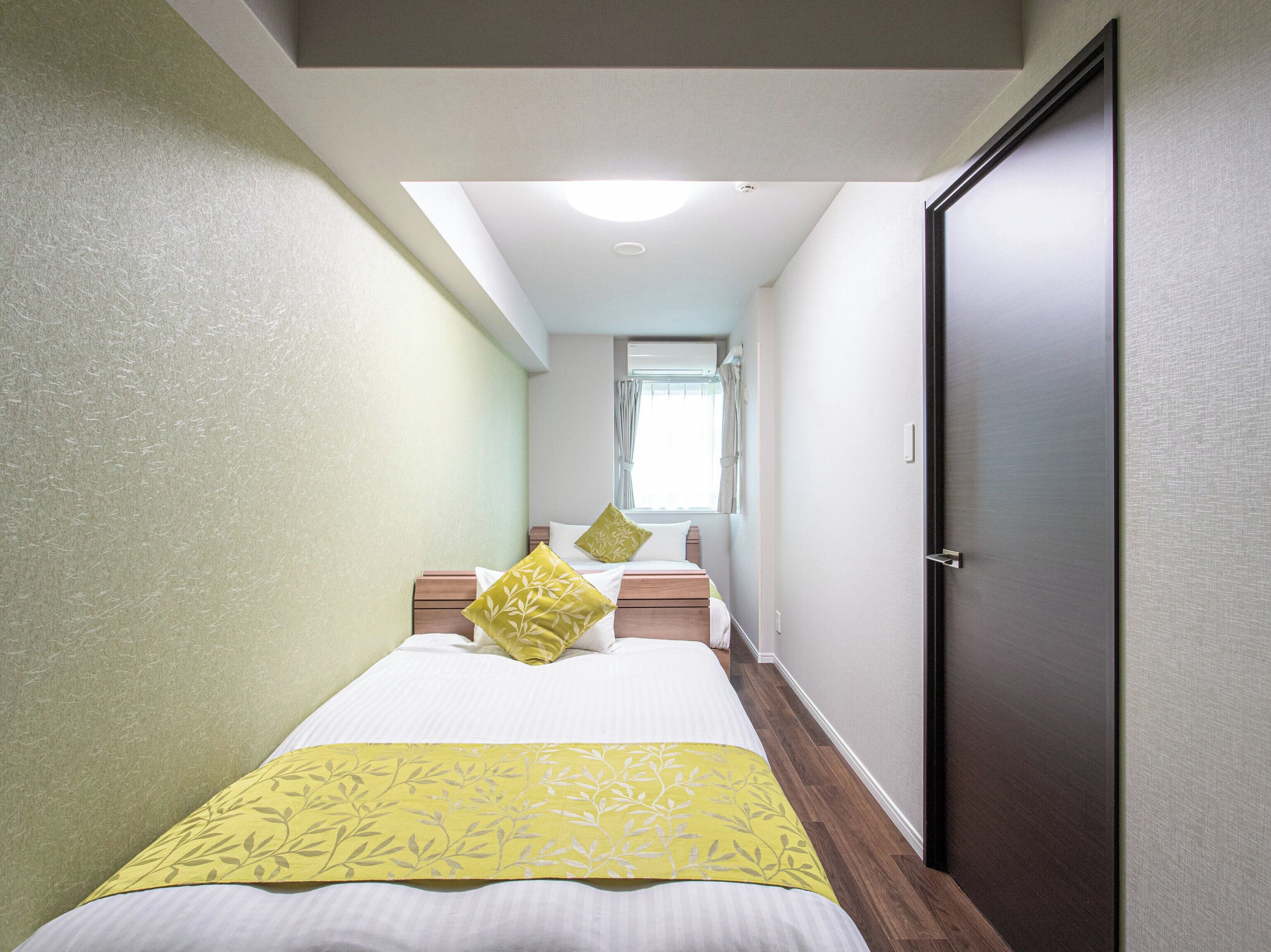 A hotel room with a bed, a window with curtains, a door, and a ceiling light.