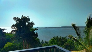 A coastal view with a clear sky, palm trees, and a calm sea. - Raposo Holiday Resort (Vagator)