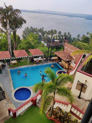 Zona de piscina con varias piscinas, un área de descanso cubierta y vista al mar.