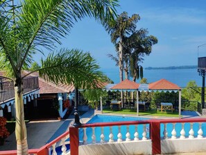A pool area with a view of the sea, surrounded by palm trees and covered seating areas. - Raposo Holiday Resort (Vagator)