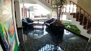 A modern lobby with a black marble floor, a staircase with wooden railings, and two black leather sofas. - Raposo Holiday Resort (Vagator)