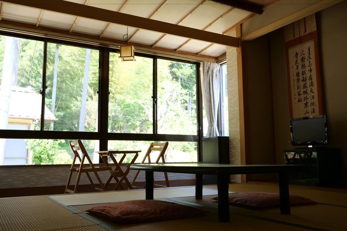 Ett traditionellt japanskt rum med tatamimattor på golvet, ett lågt bord och utsikt över grönskan utanför.