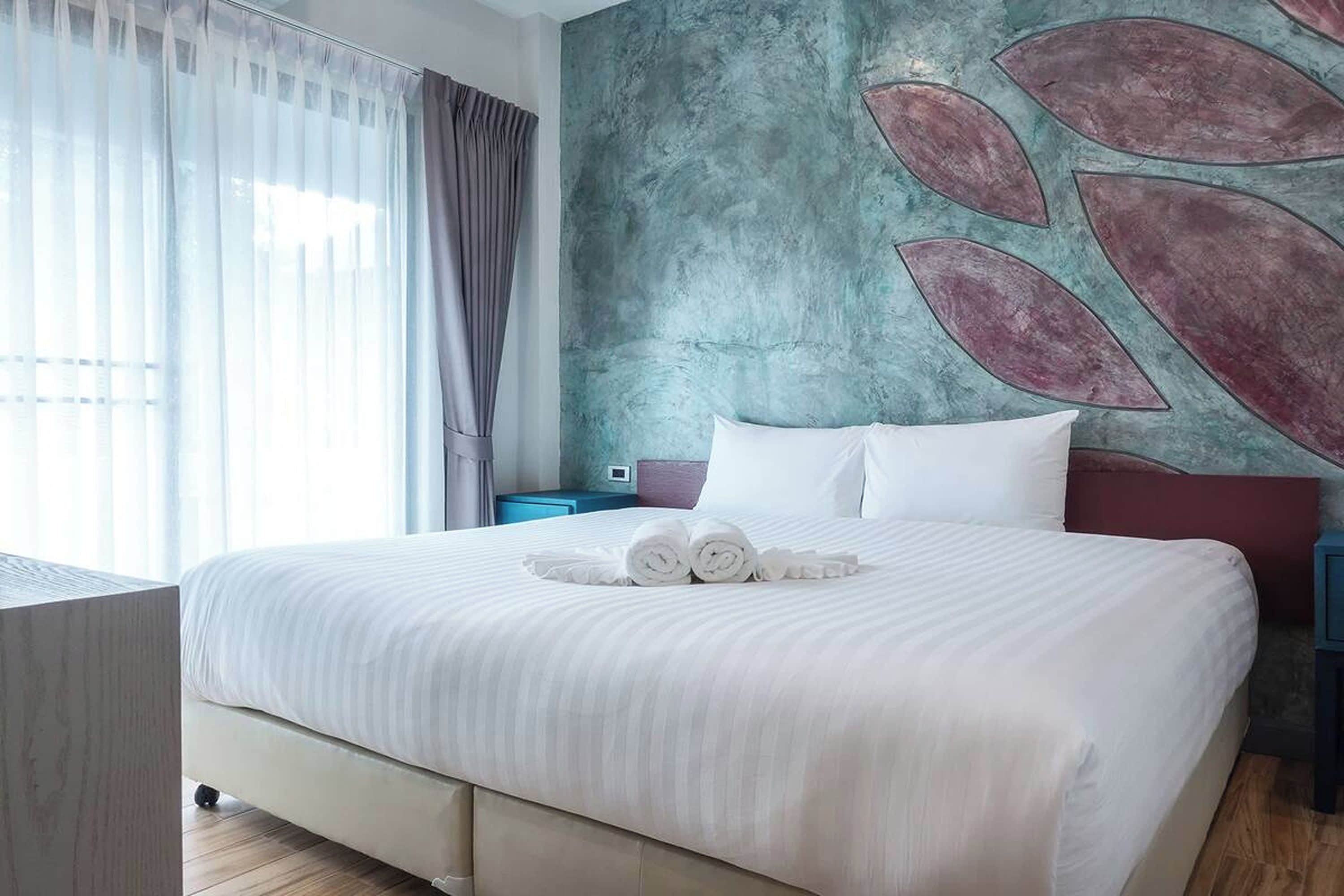 Ein Hotelzimmer mit einem großen Bett, einem Nachttisch, einem Schreibtisch und Blick ins Freie.