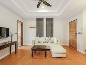 A living room with a sofa, a coffee table, a TV, and a ceiling fan. - Coco Retreat Phuket Resort and Spa Sha+ (Chalong)
