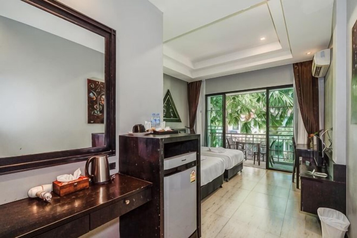 A hotel room with a bed, a desk, a chair, a window with a view of greenery, and a balcony.