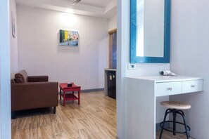 A room with a brown sofa, a small red table, a white vanity with a mirror, and a wooden floor. - Coco Retreat Phuket Resort and Spa Sha+ (Chalong)