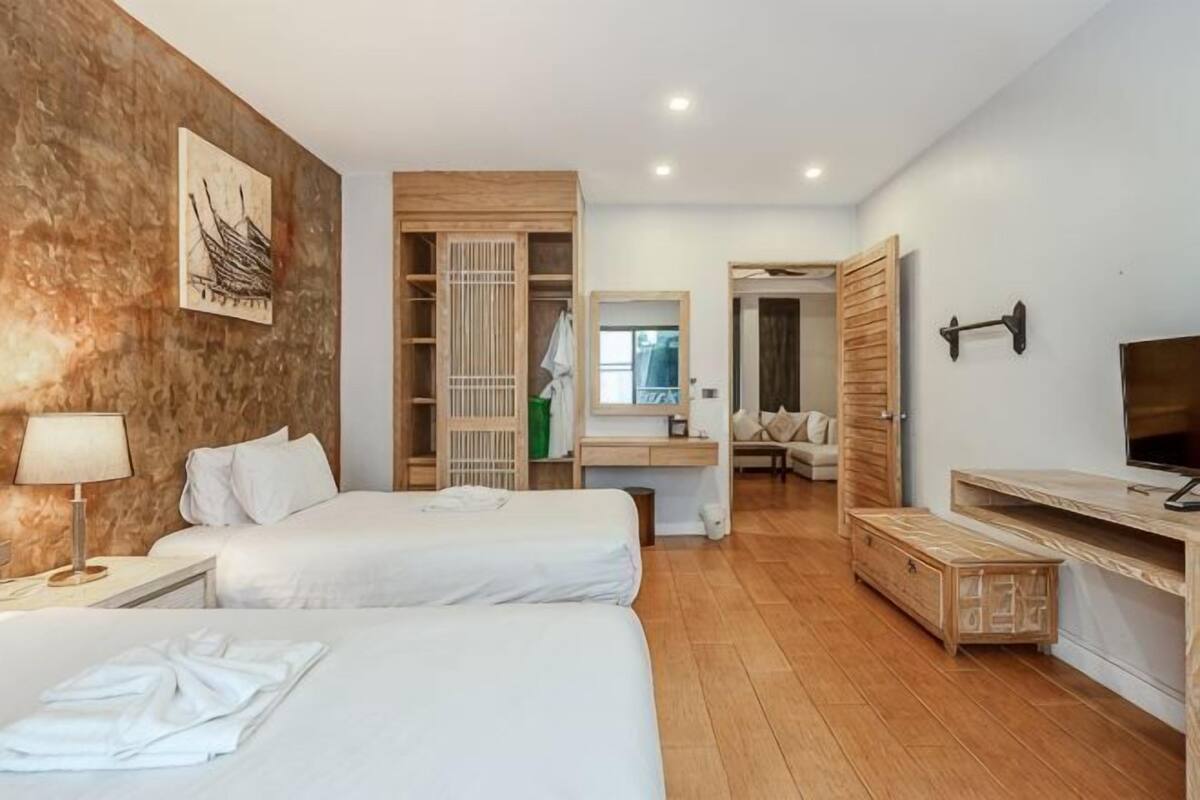 Habitación de hotel con dos camas, un armario de madera, un televisor, un espejo y un banco de madera.