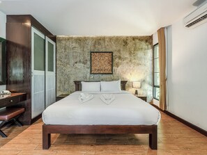 Hotellihuone, jossa on suuri sänky, puinen penkki, työpöytä ja kiviseinä, jossa on koristeellinen paneeli.