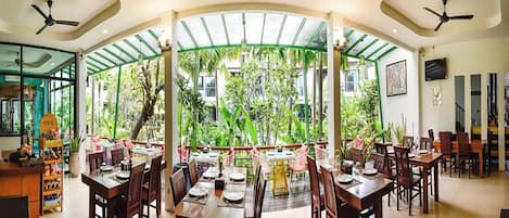 Un restaurante con varias mesas y sillas, una barra y vistas a zonas verdes a través de un recinto de cristal.
