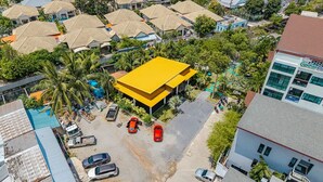 An aerial view of a residential area with multiple houses, a yellow-roofed building, and parked cars. - Coco Retreat Phuket Resort and Spa Sha+ (Chalong)