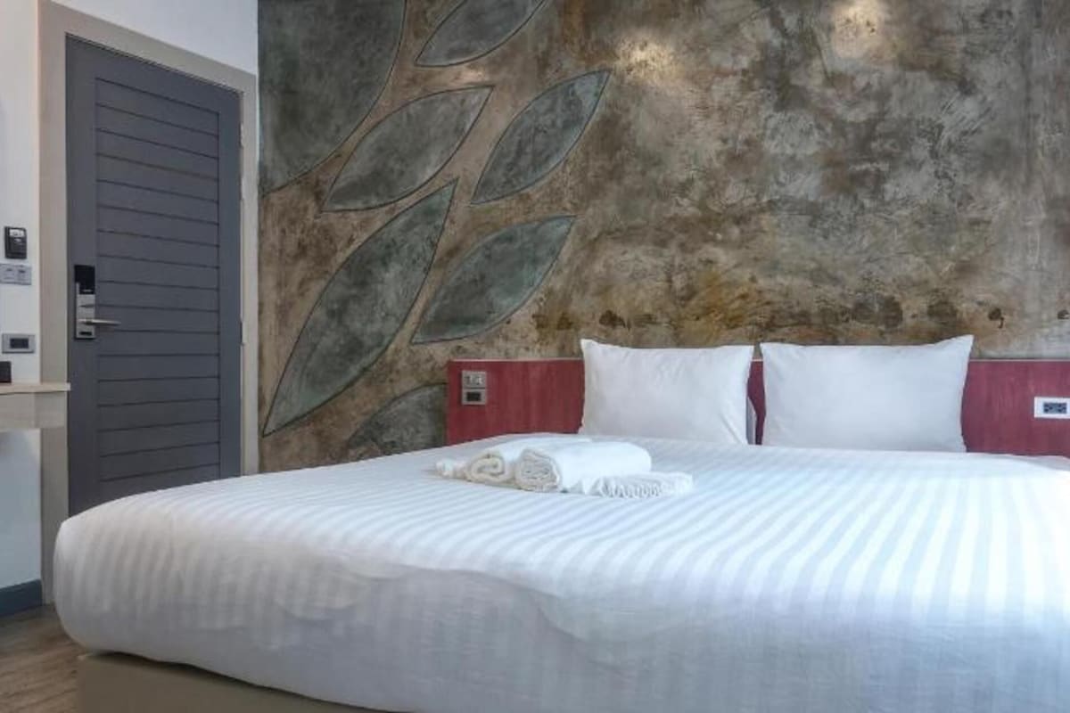 A hotel room with a bed, a wall with leaf patterns, a door, and a small table.