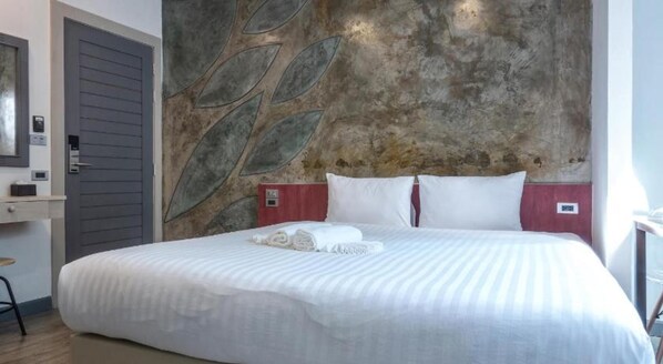 Quarto de hotel com cama, parede com desenhos de folhas, porta e uma pequena mesa.