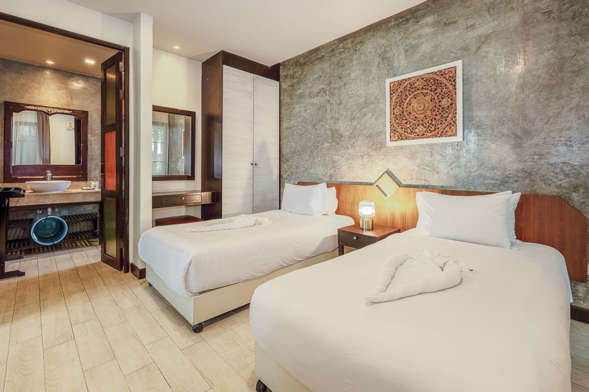 A hotel room with two beds, a bathroom with a sink and mirror, and a decorative wall piece.