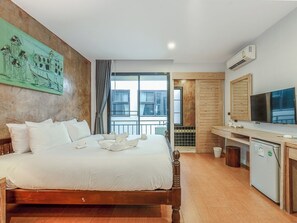 Hotellihuone, jossa on sänky, televisio, pieni keittokomero ja suuri ikkuna.