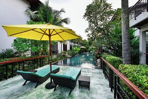 A poolside area with lounge chairs and a yellow umbrella, surrounded by lush greenery and a pool. - Coco Retreat Phuket Resort and Spa Sha+ (Chalong)