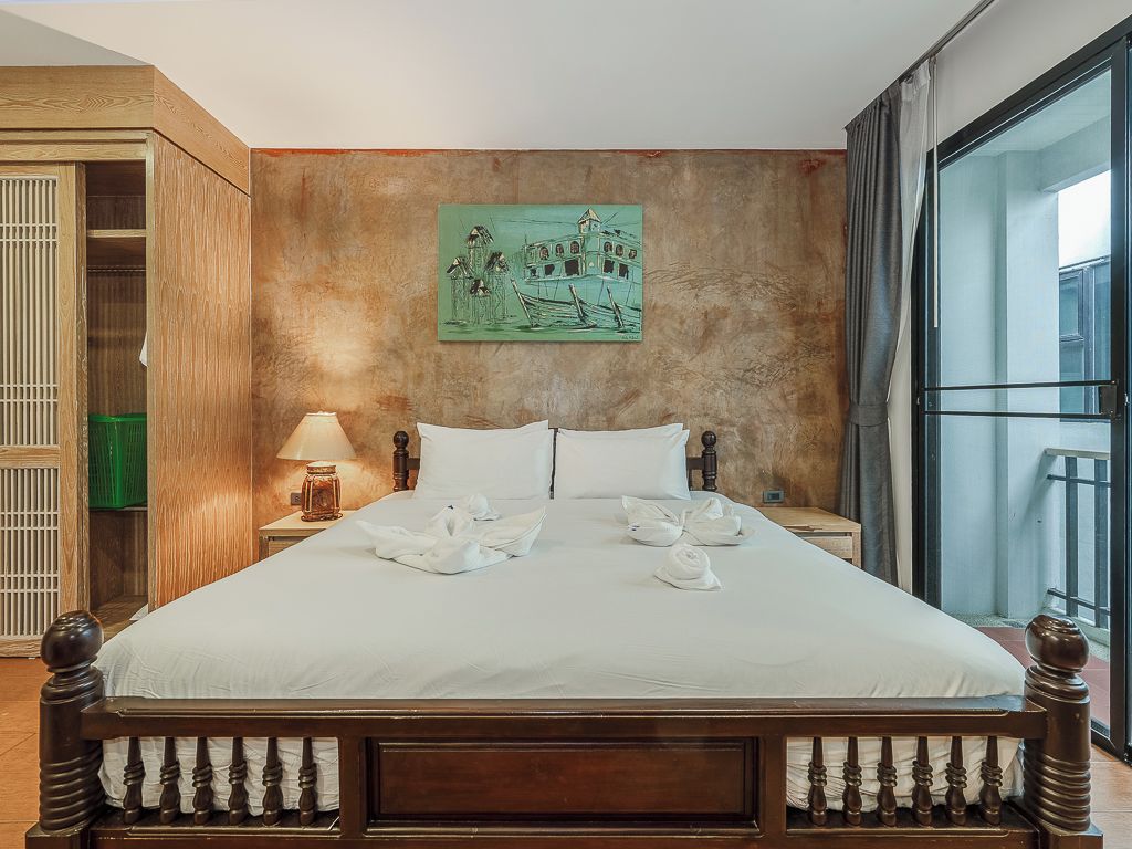 A hotel room with a large bed, a painting on the wall, a window with curtains, and a wooden wardrobe.