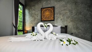 A neatly made bed with towels arranged in swans and flowers, a wall with a decorative panel, and a window with greenery visible. - Coco Retreat Phuket Resort and Spa Sha+ (Chalong)