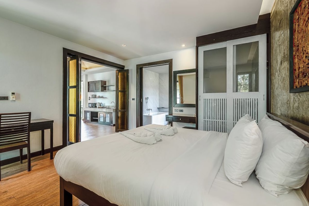 Un dormitorio con una cama grande, un escritorio y una silla. Se ve un baño a través de una puerta abierta.
