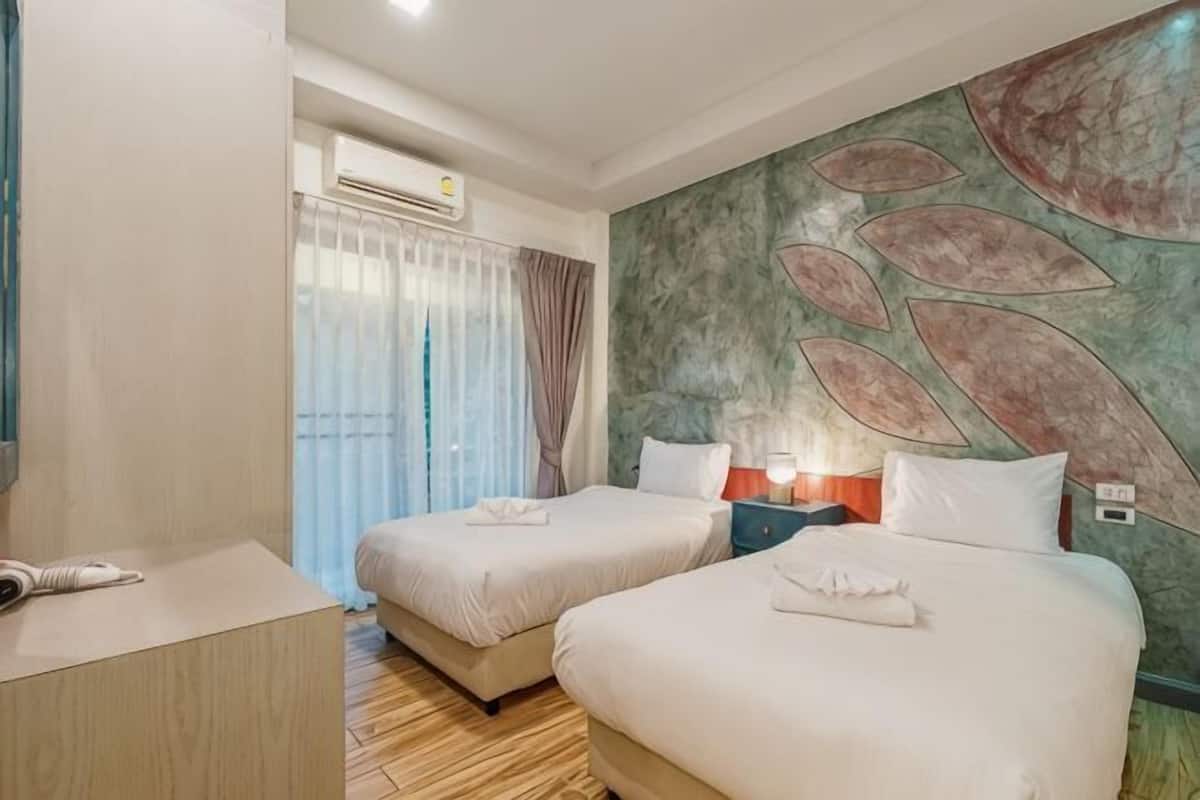 Habitación de hotel con dos camas, un escritorio, aire acondicionado, una ventana con cortinas y una pared con diseño de hojas.
