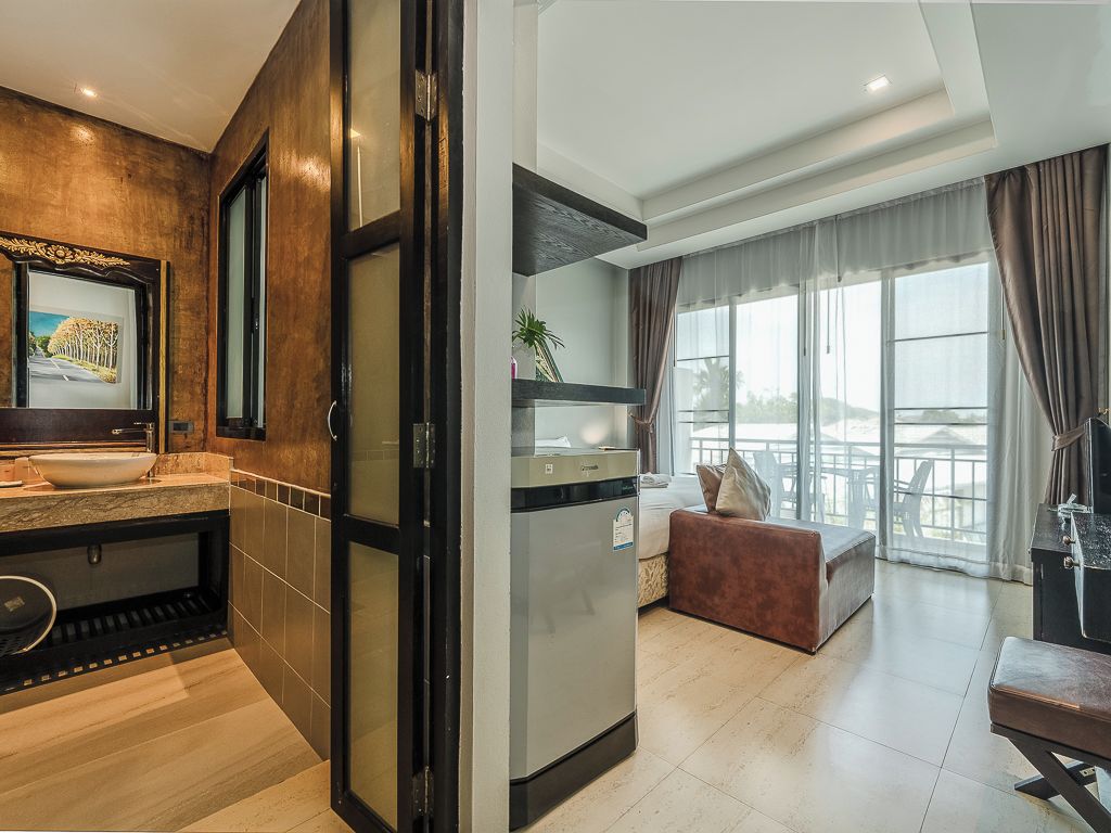 A modern hotel room with a kitchen area, a living space with a sofa and a dining table, and large windows offering a view.